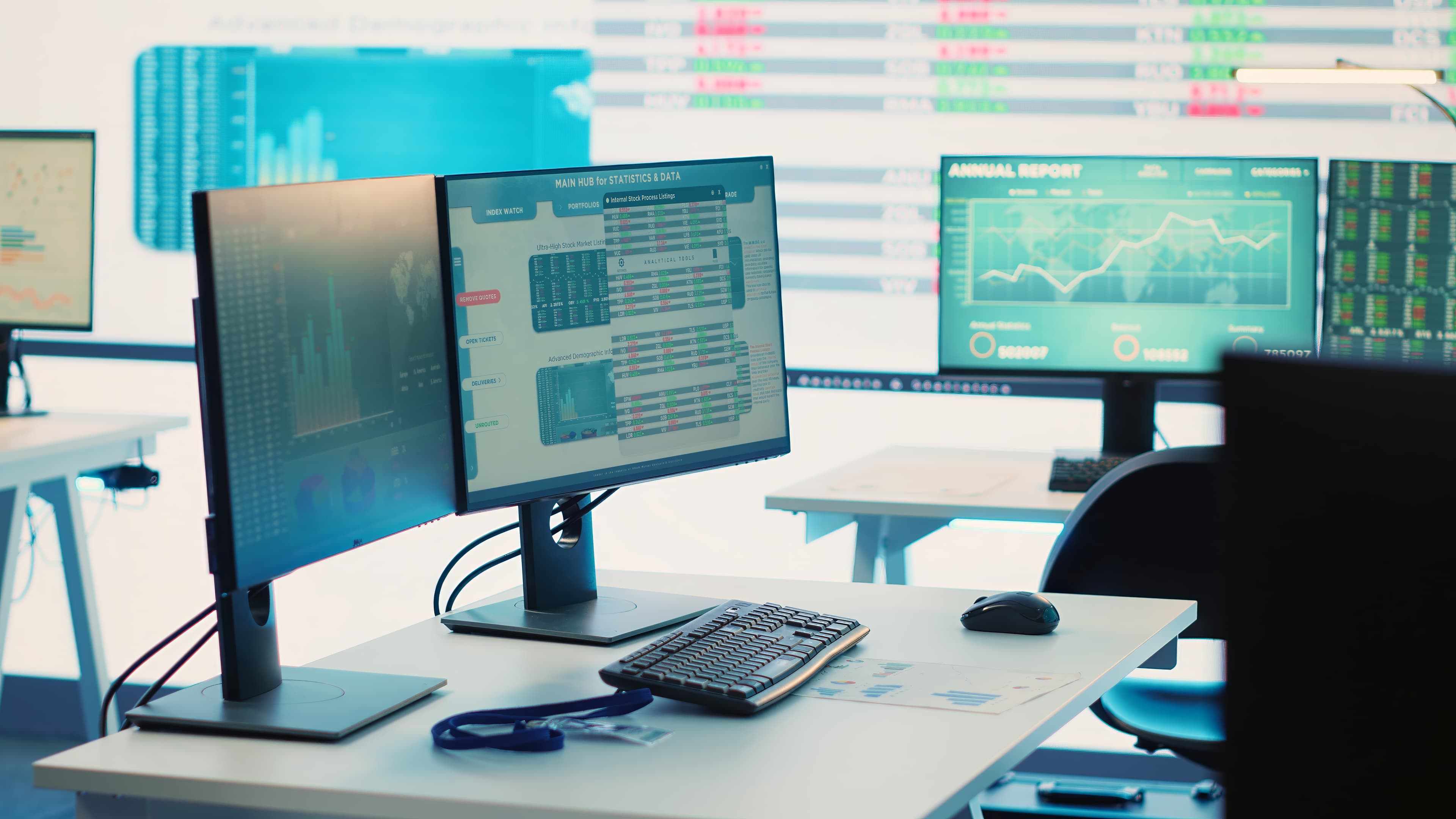 A modern data operations desk with multiple monitors displaying live analytics dashboards, with a large data screen wall in the background.